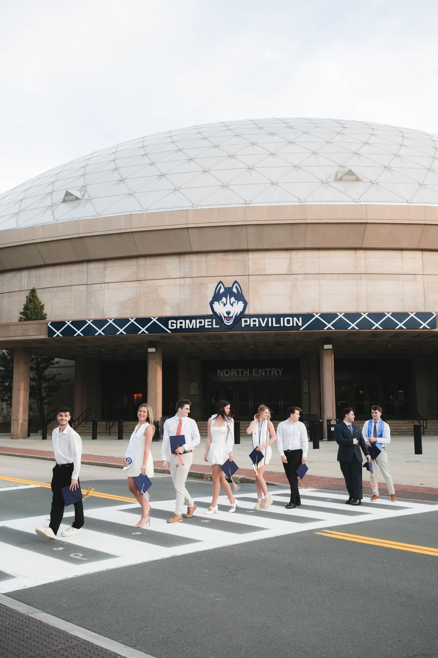 UConn student graduates walk on sidewalk in front of Gampel building