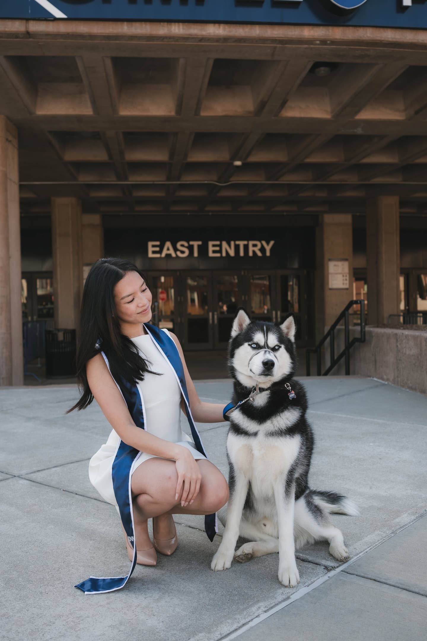 UConn student posing with Jonathan the husky in front of Gampel Pavilion