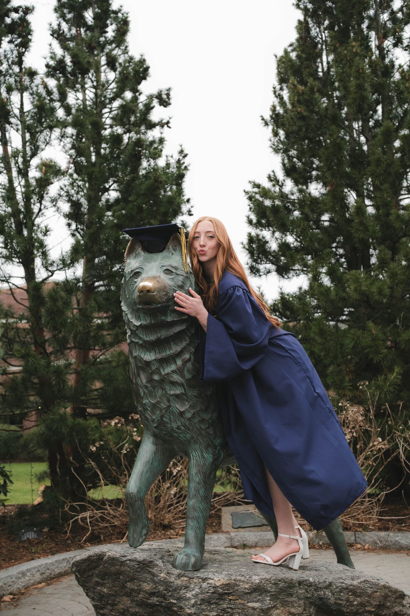 UConn student graduate striking a pose next to the Jonathan the Husky statue