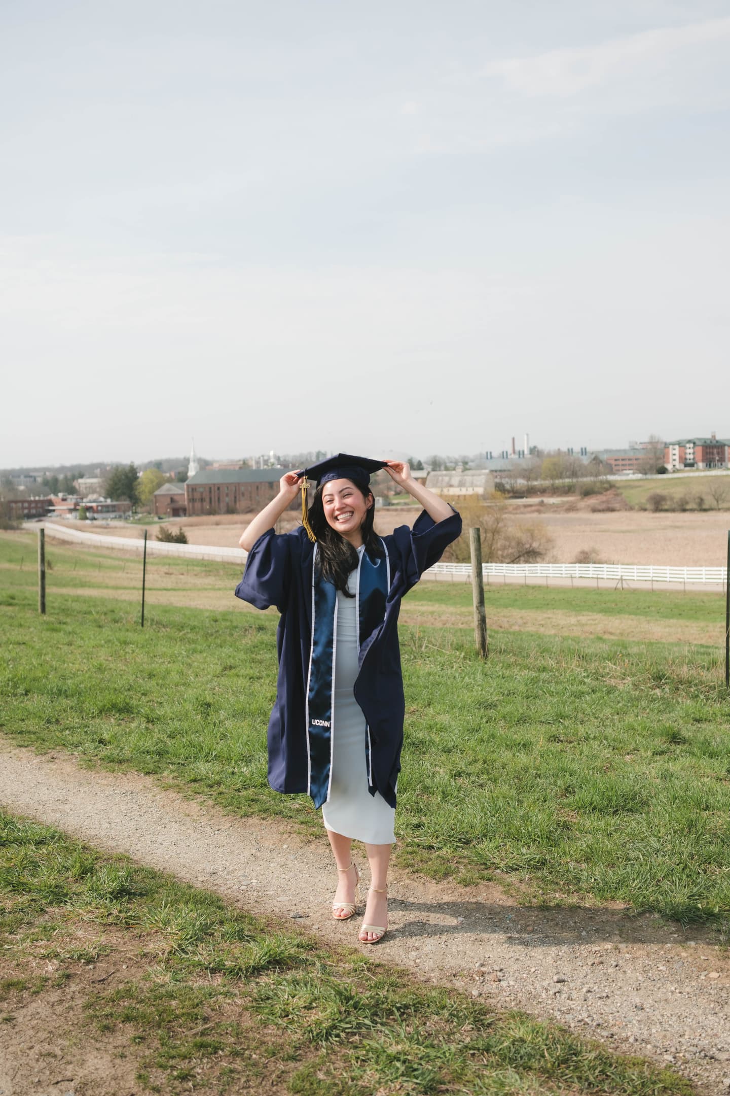 UConn student graduate poses for photo on Horsebarn Hill with campus in background